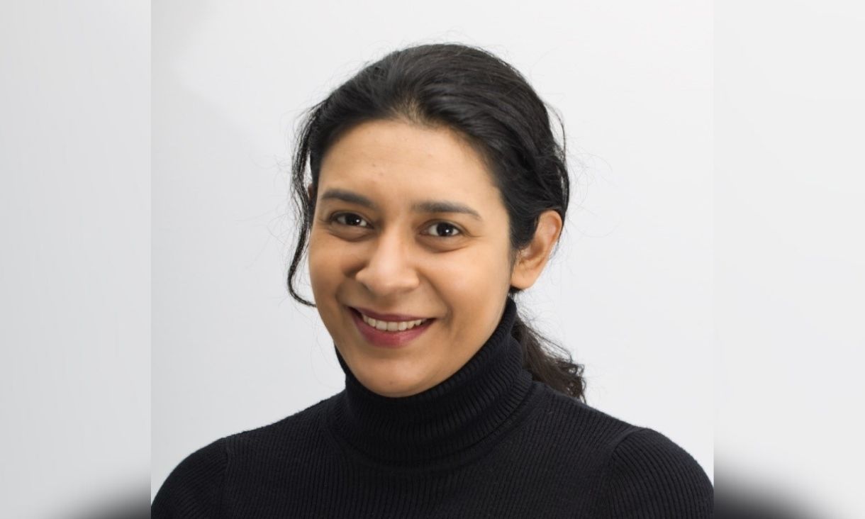Dr Jessica Rivera Villicana is smiling in a black high-neck top in front of a white background.