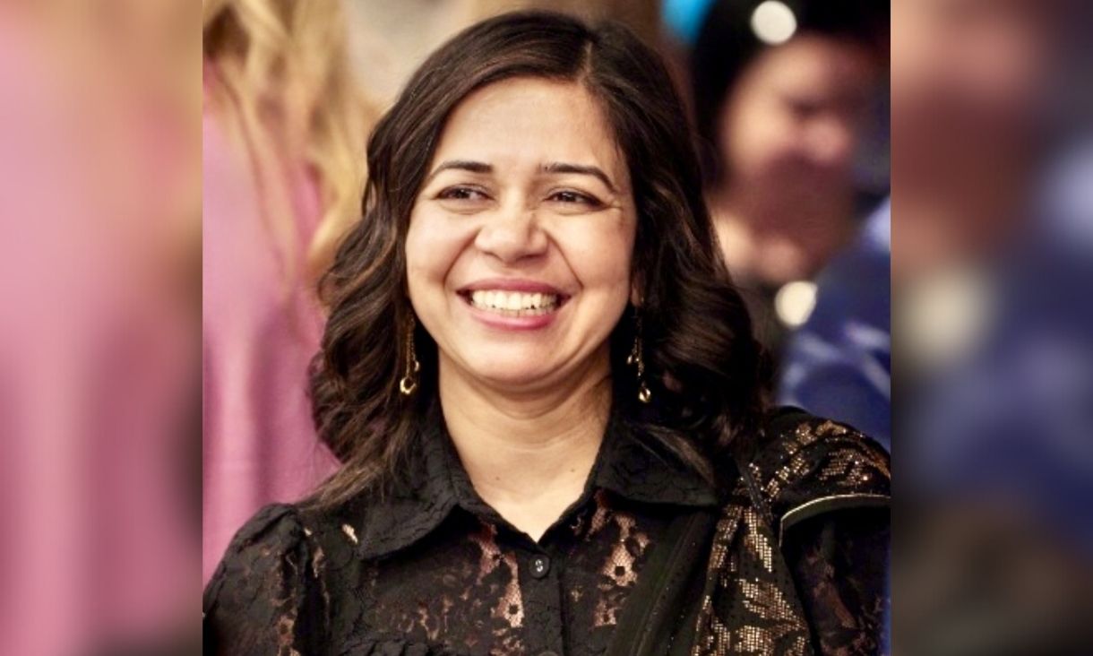 Associate Professor Sonika Tyagi is smiling in a black dress with lots of brightly coloured dressed people blurred in the background.