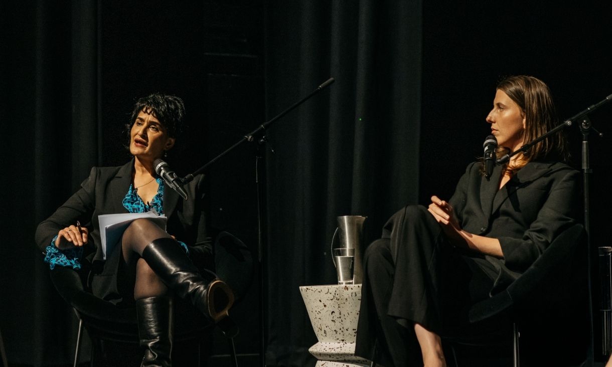 two women sit on stage with mics in conversation