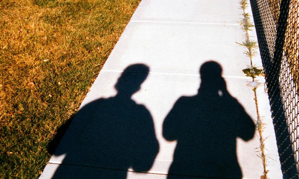 shadows, one holding a camera, are projected onto pavement 