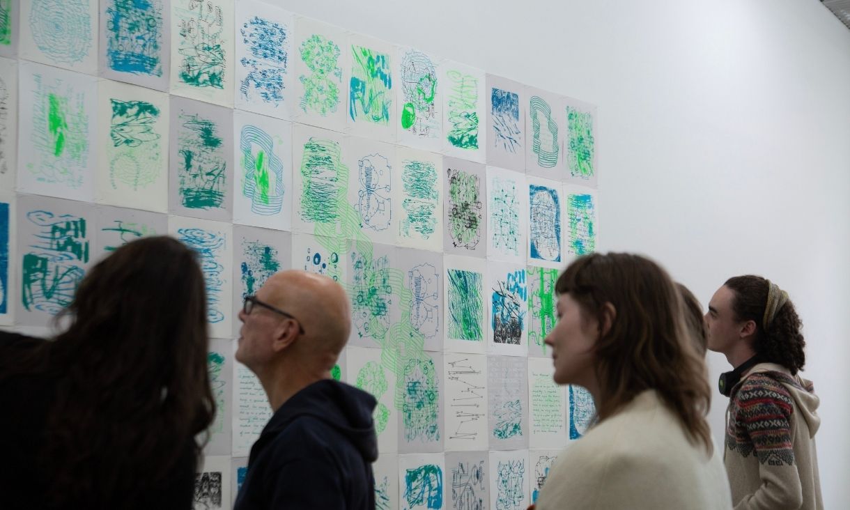 A large group on onlookers admire the studio's work in the gallery space.