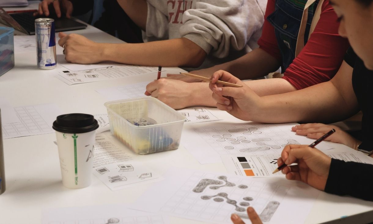students sit in a group, coffee and energy drinks around them as they draw ideas for MDW.