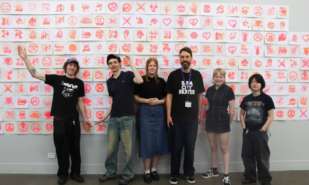 Six people wearing black line up against a wall of hit pink and neon orange prints.
