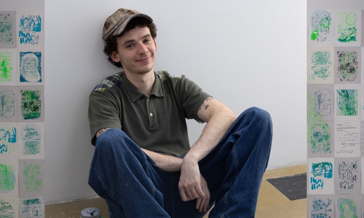 Will sits against a white wall and is smiling at the camera.
