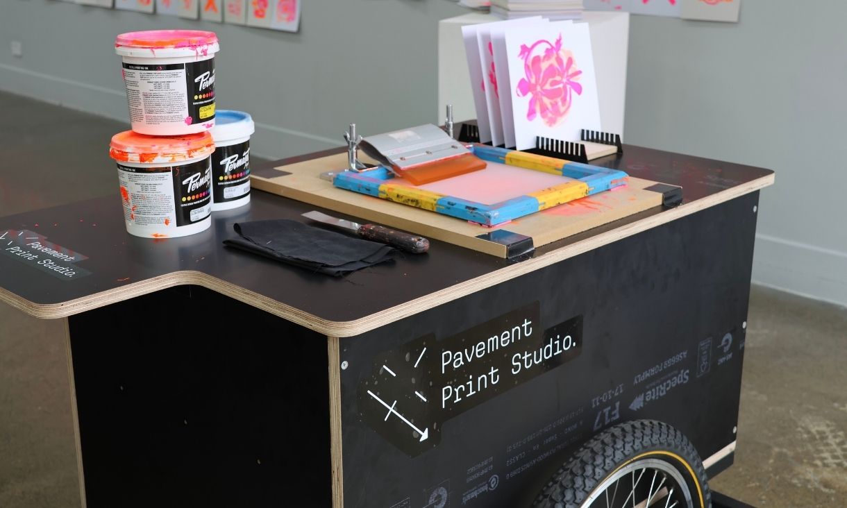 A bike trailer with Pavement Print Studio logos engraved into it, it has lots of permaset inks and merchandise made by students.