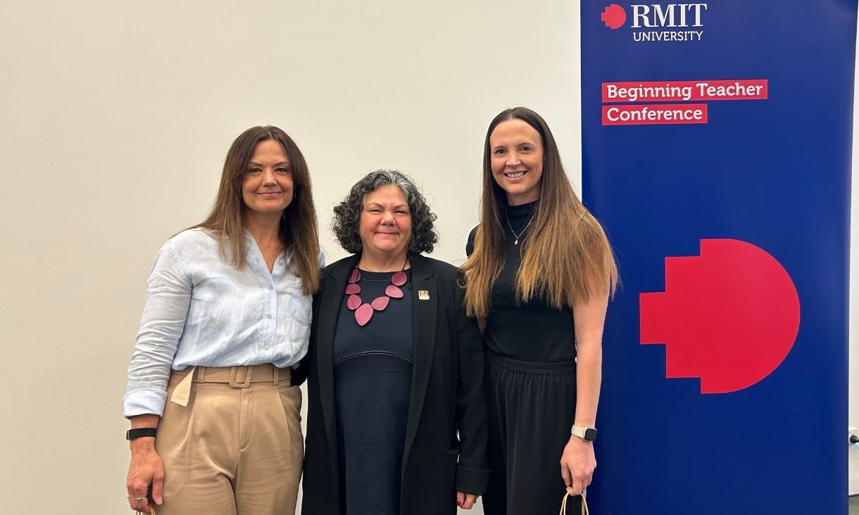 three women stand together in front of an RMIT banner