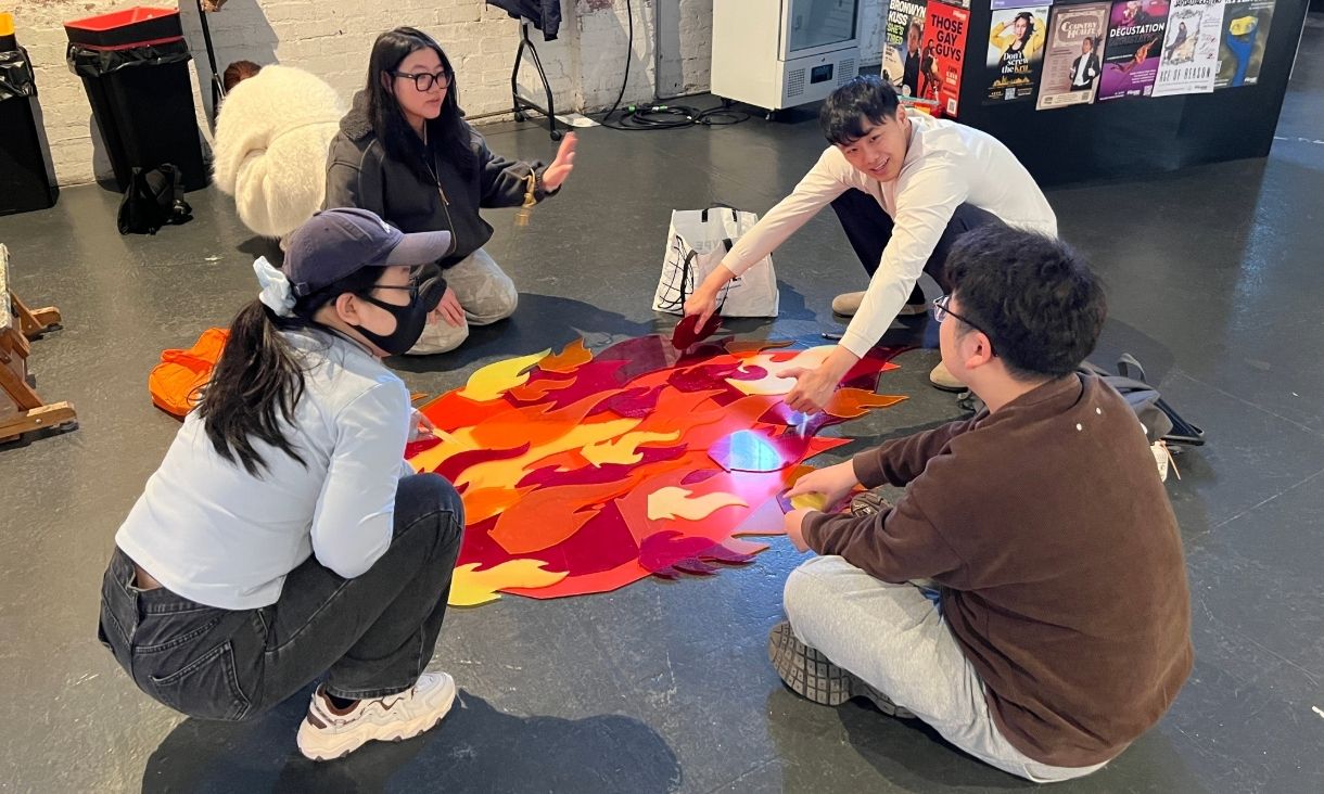 Students crouch by a flat lay of art depicting flames 