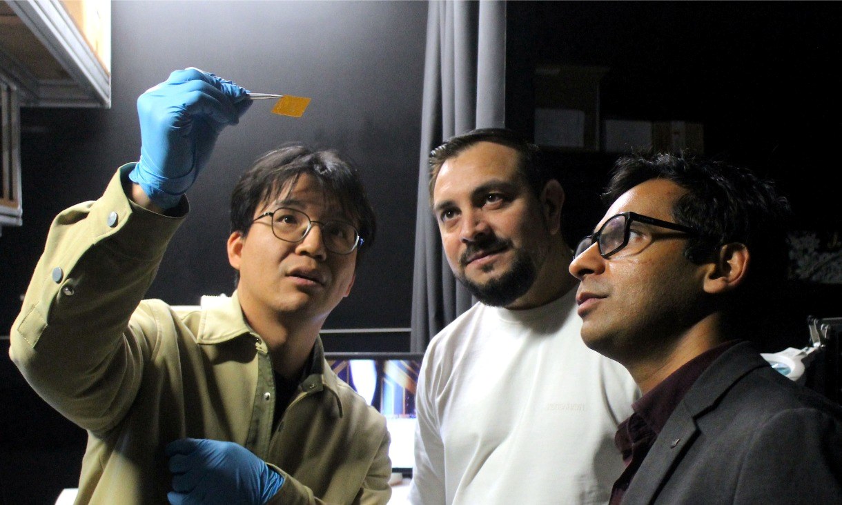 Three researchers standing alongside laboratory equipment while examining a component used in the neuromorphic vision project.