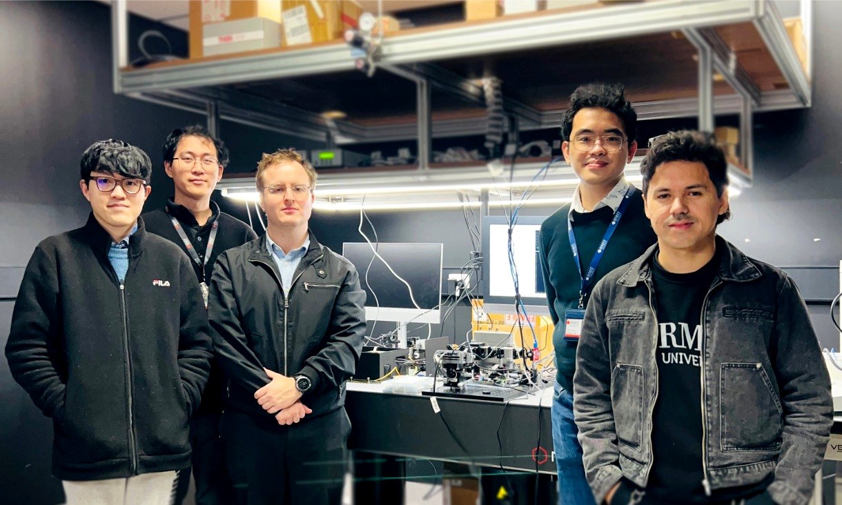 Group photograph of researchers standing in a laboratory surrounded by electronics and testing equipment associated with the neuromorphic vision project.