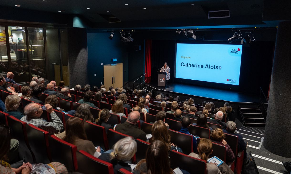 A person speaks on a stage in front of a large audience