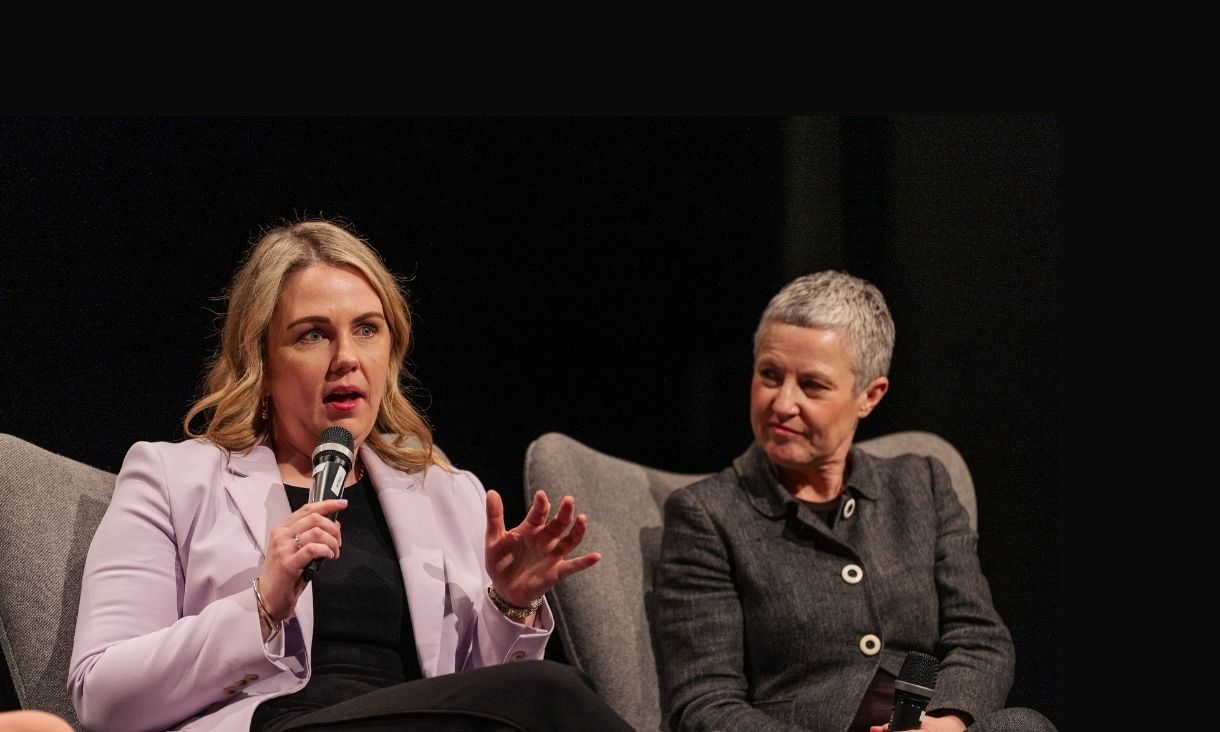 Two people speak on a panel with a mic