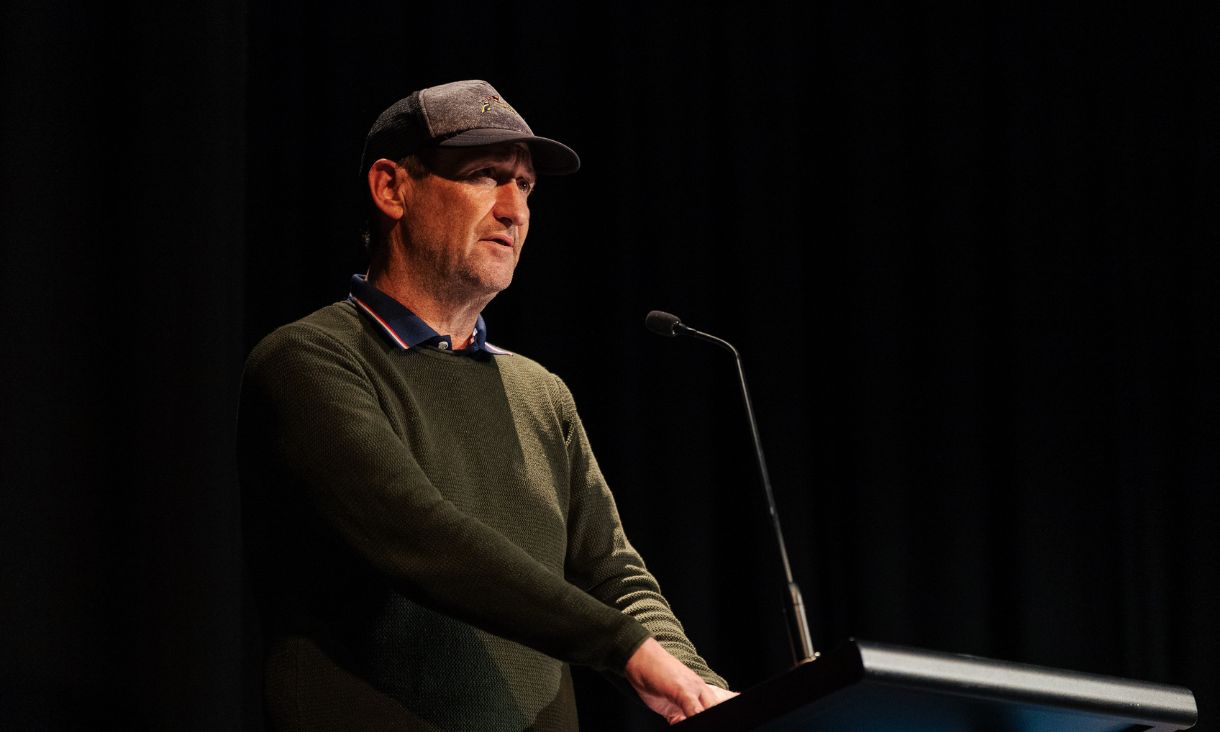 A person speaks at a podium, with a spotlight shining on them dramatically