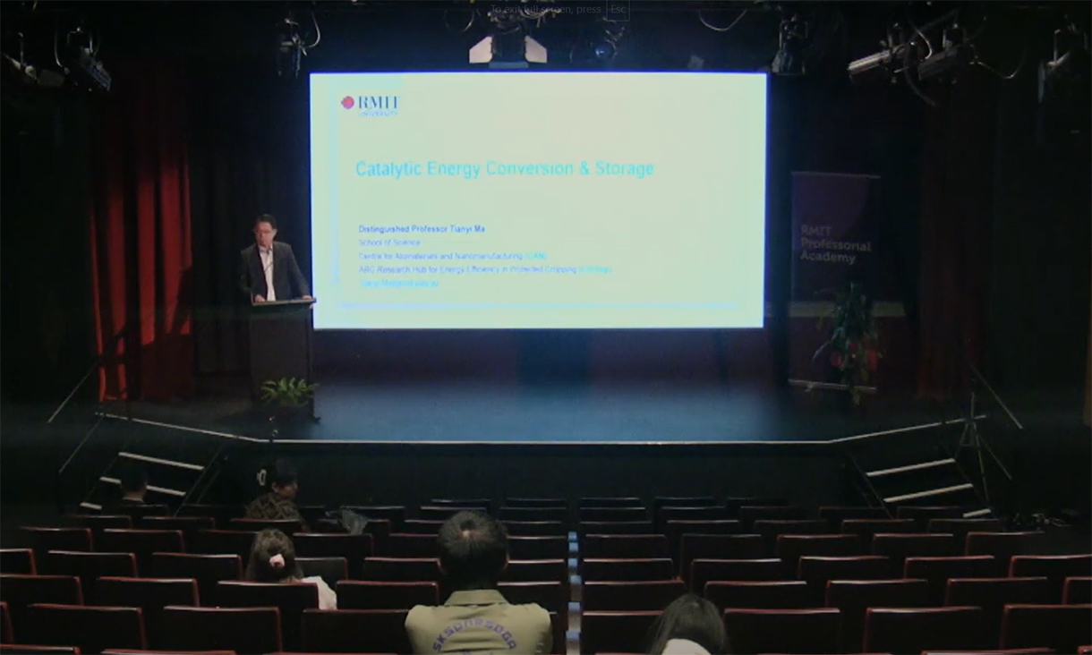 A lecture theatre with a screen behind the speaker