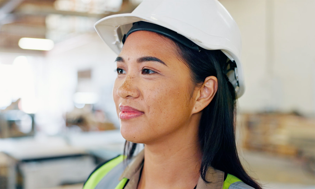 Construction workers in safety gear working inside a partially built commercial building with scattered tools, debris, and sunlight streaming through large windows.