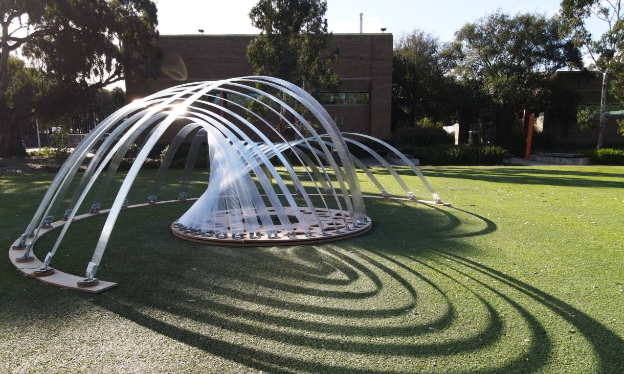 outdoor photo of kinetic pavilion, a  geometric curved synthetic structure on a lawn