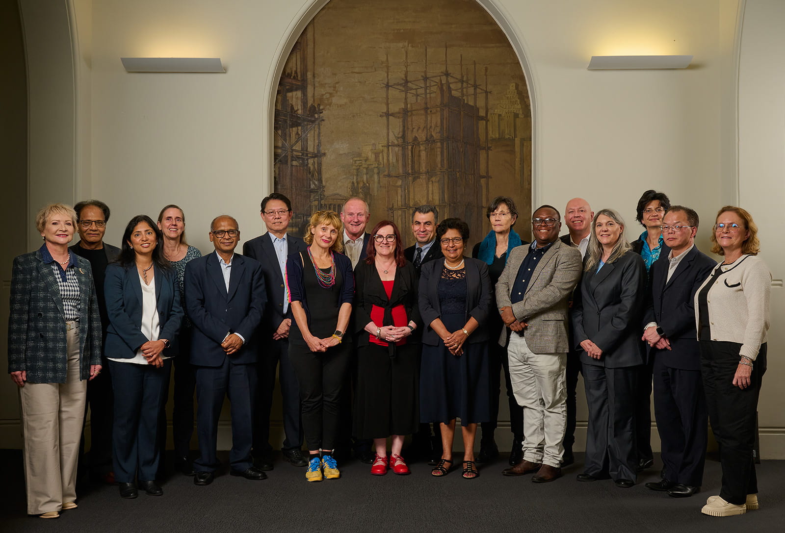 A group of professors standing indoors in front of an arched fresco.