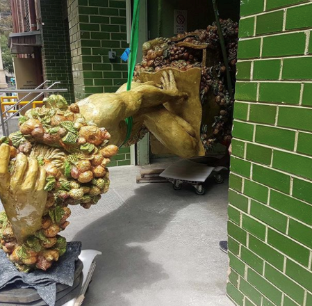 A large sculpture of a nude male figure covered in garlands of fruit an foliage is laid on its side to enter the Gallery's loading dock