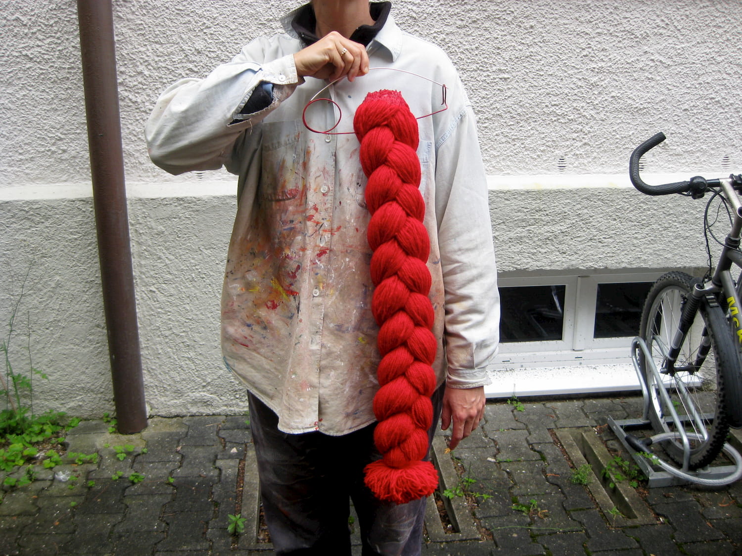 A photo of a person wearing a paint-spattered white shirt, holding a thick, long, red wool braid