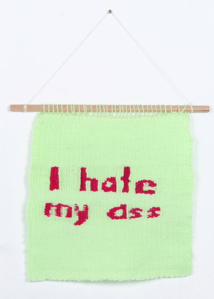 A pale green square of fabric with dark pink writing 'I Hate My Ass'
