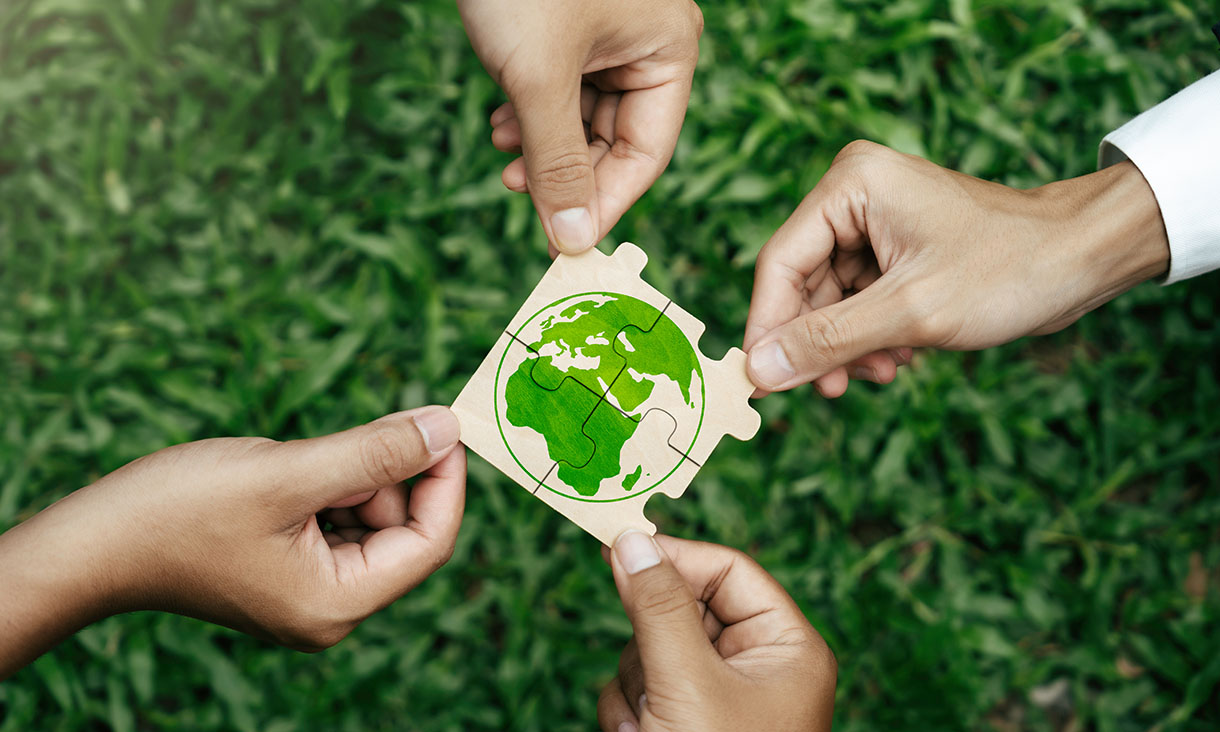 Hands holding puzzle pieces together forming an image of the Earth with a green background.