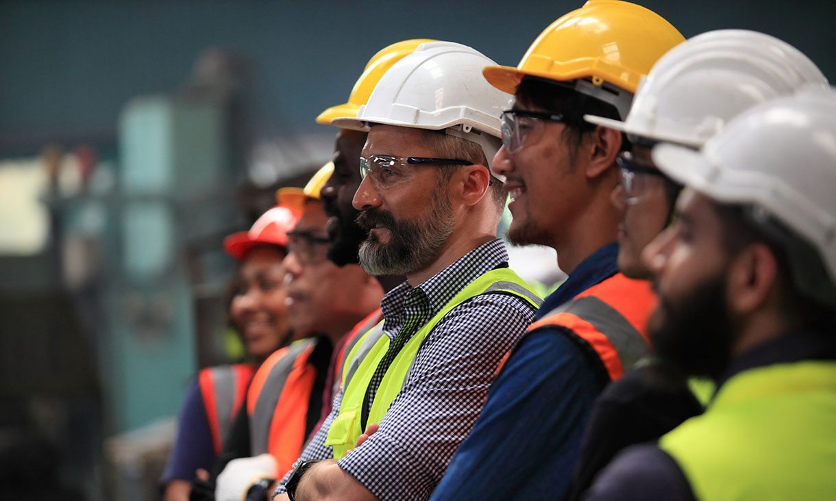 Group of engineers in hard hats and safety vests listening attentively during a workplace session.