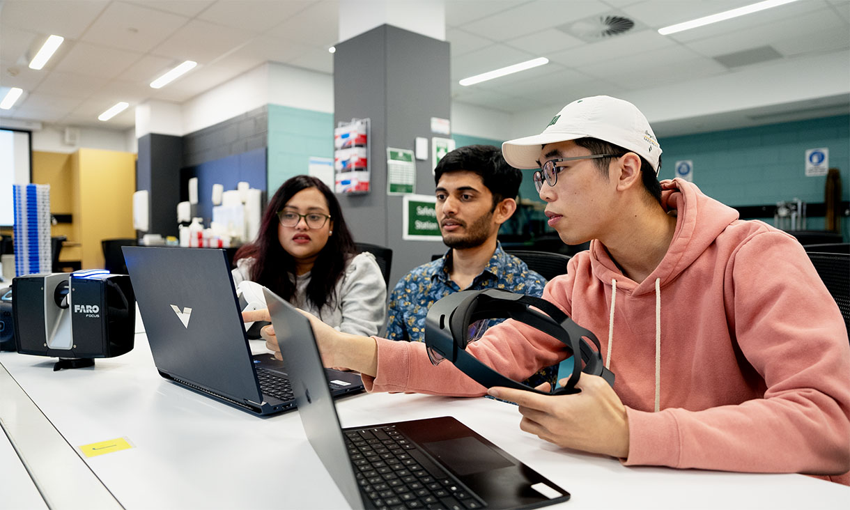 Students using laptops and a VR headset while working together in a classroom.