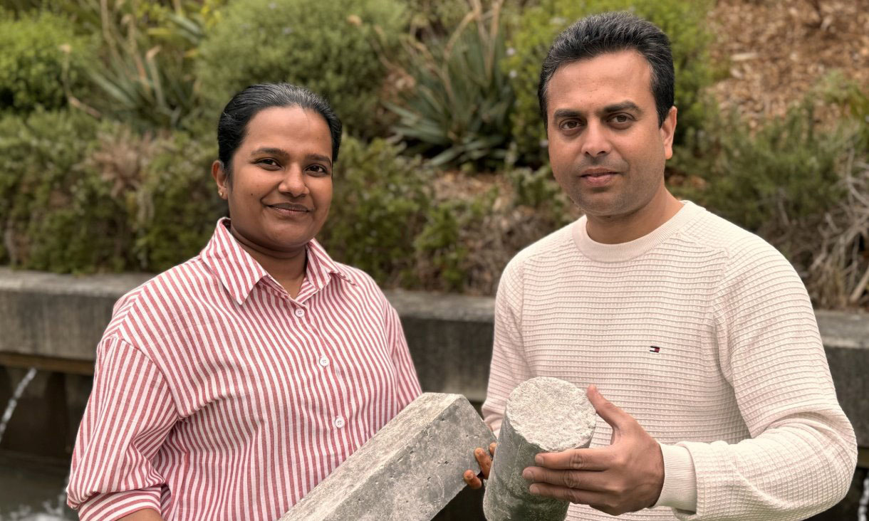 Two researchers outdoors holding samples of concrete material.