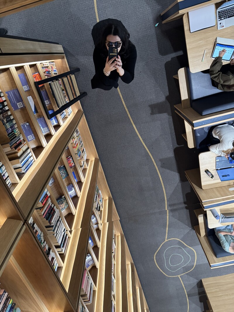 Overhead view of a person taking a photo in a library, with bookshelves and study desks nearby, capturing a modern learning environment.