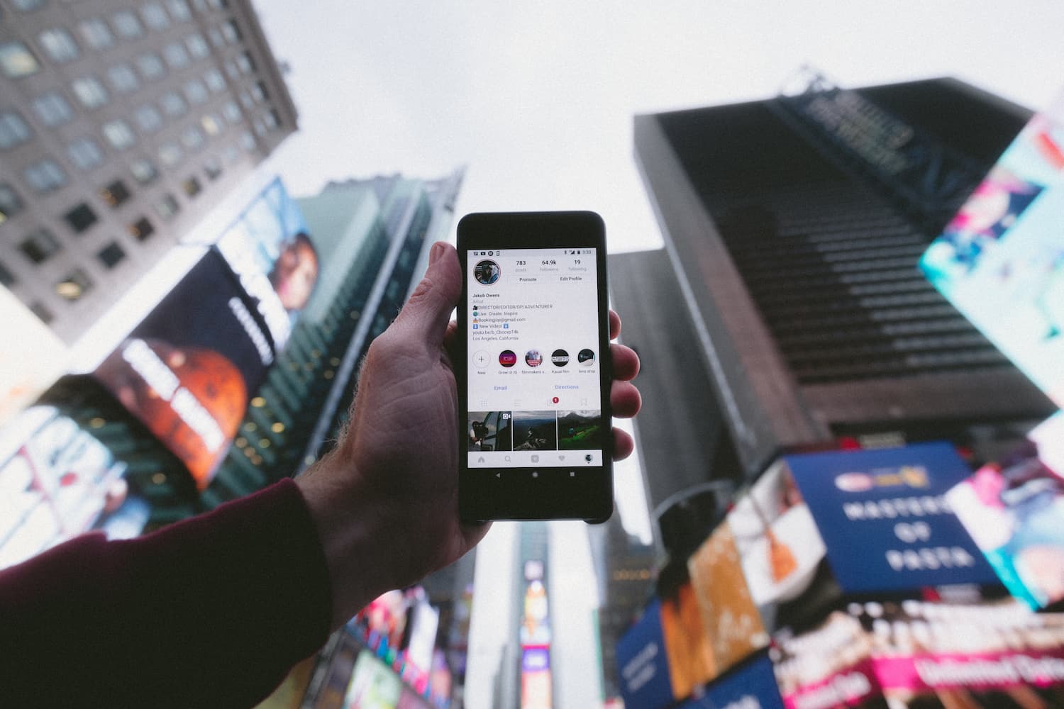 A hand holding phone with Instagram on screen against background of skyscrapers