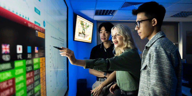 Three students using an interactive screen with graphs and financial data.