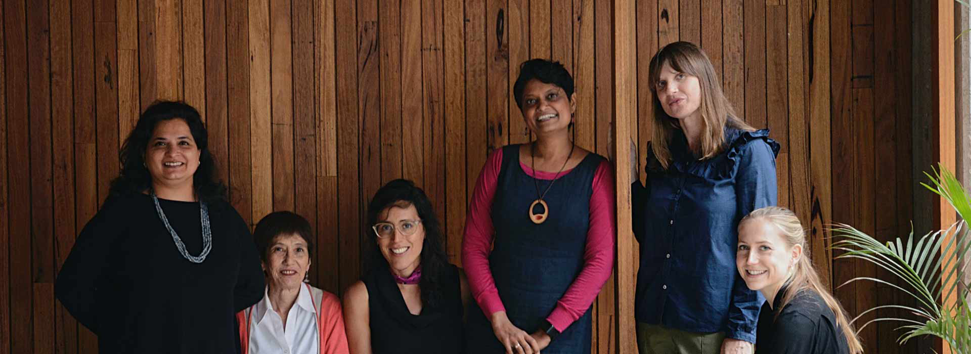 Six women in front of a wooden wall and smiling at the camera
