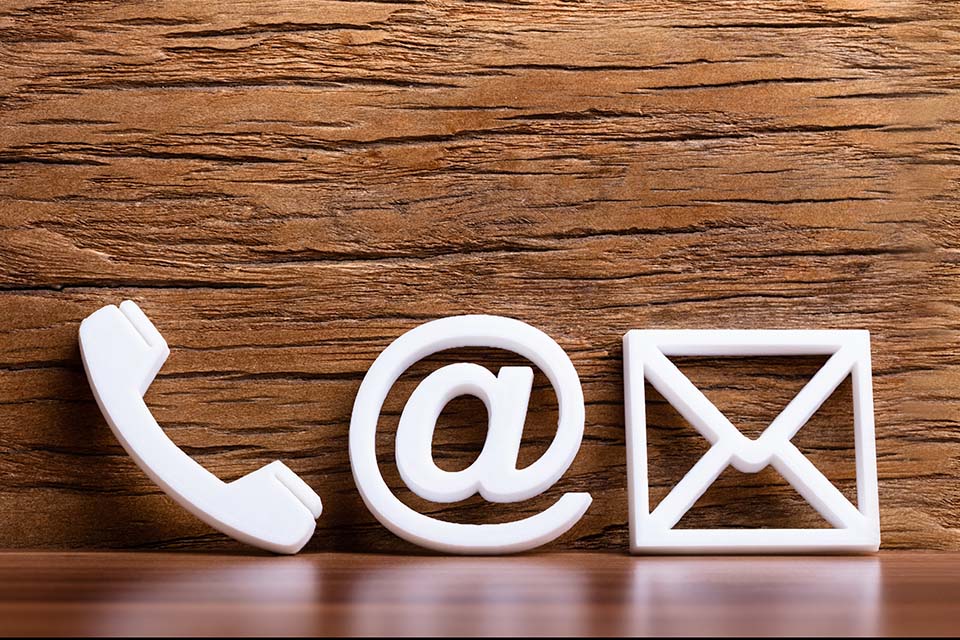 Image of three white contact icons. These include a telephone, the at symbol and mail symbol.. The background features a brown wooden texture.