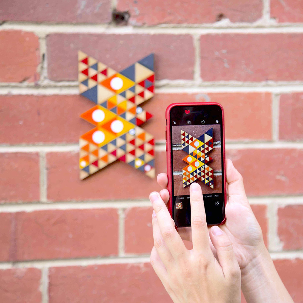 A person taking a photo of artwork on a brick wall, using a phone