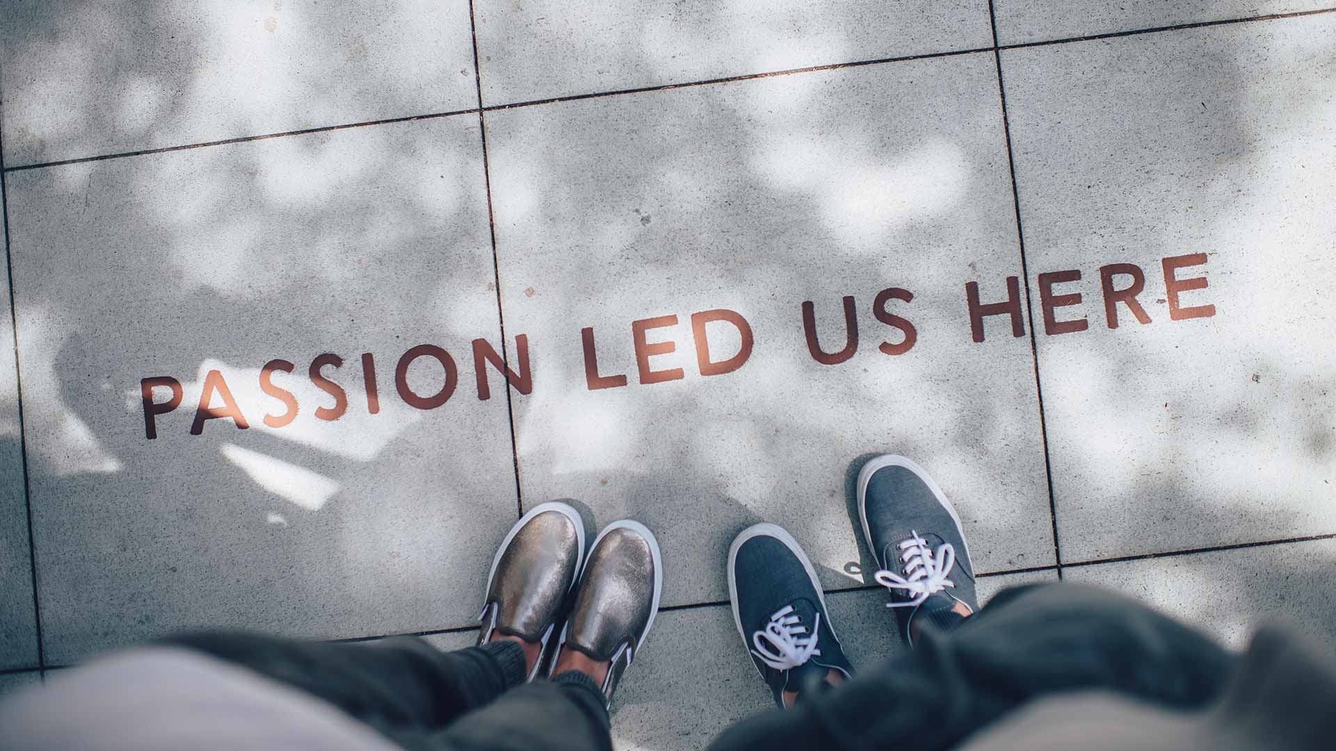 Two people standing on concrete in front of the words 'Passion led us here'