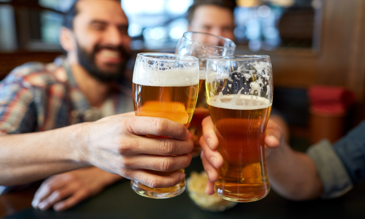 three glass of beers being held together, with two men blurry in background