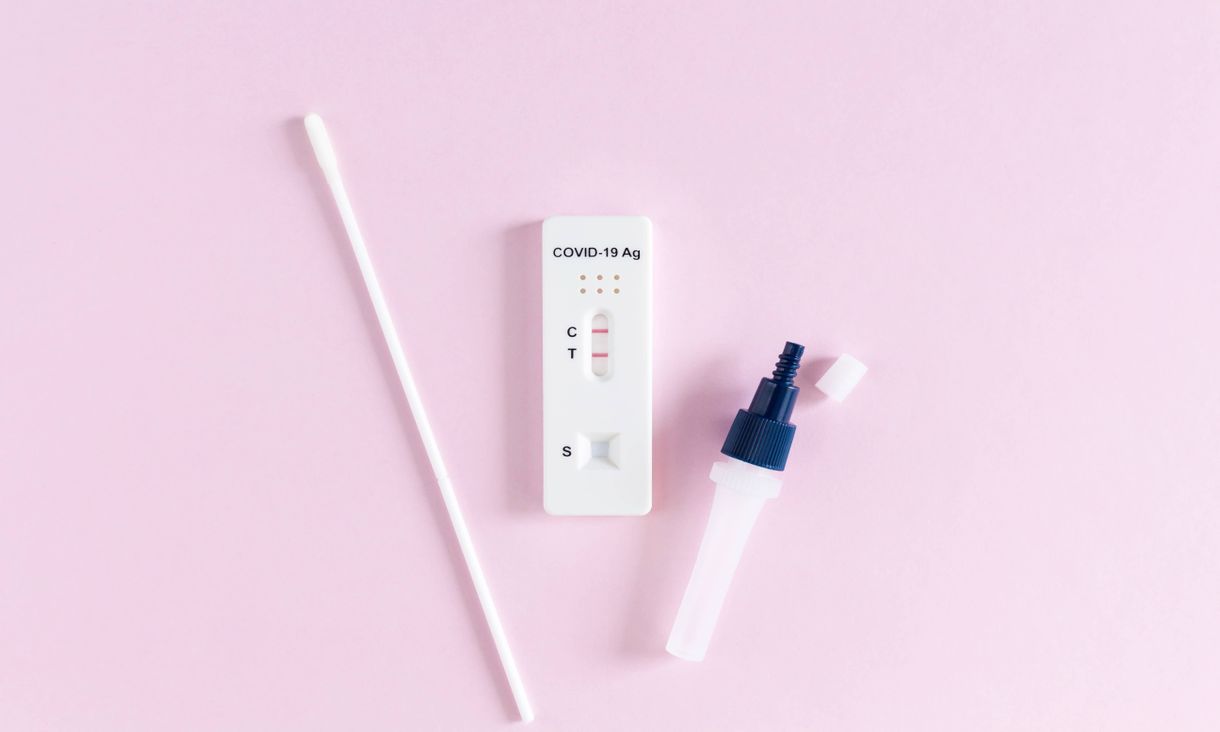 positive rapid antigen test with swab and vial against pink background