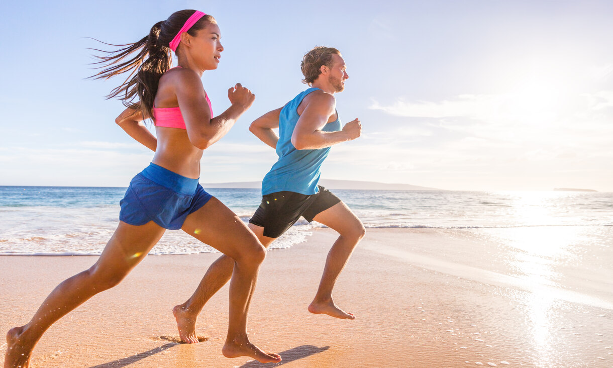 male and female joggers running on beach