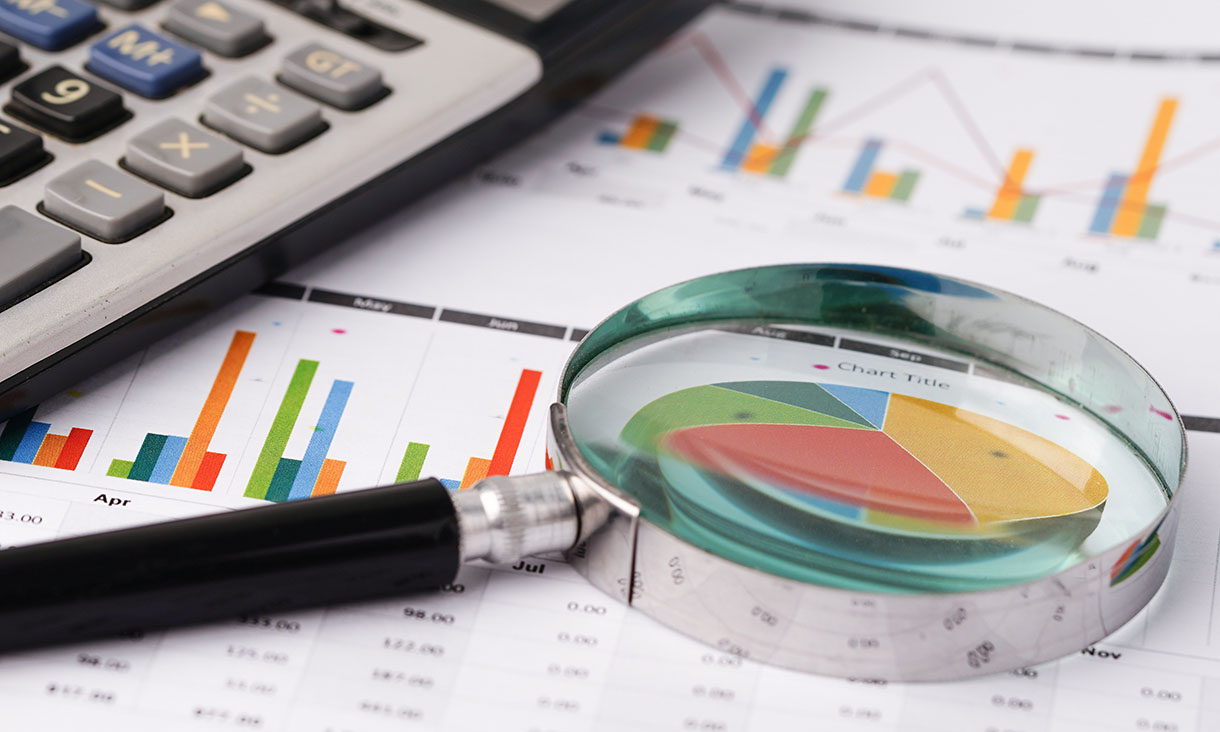 A magnifying glass and a calculator lying atop some spreadsheets