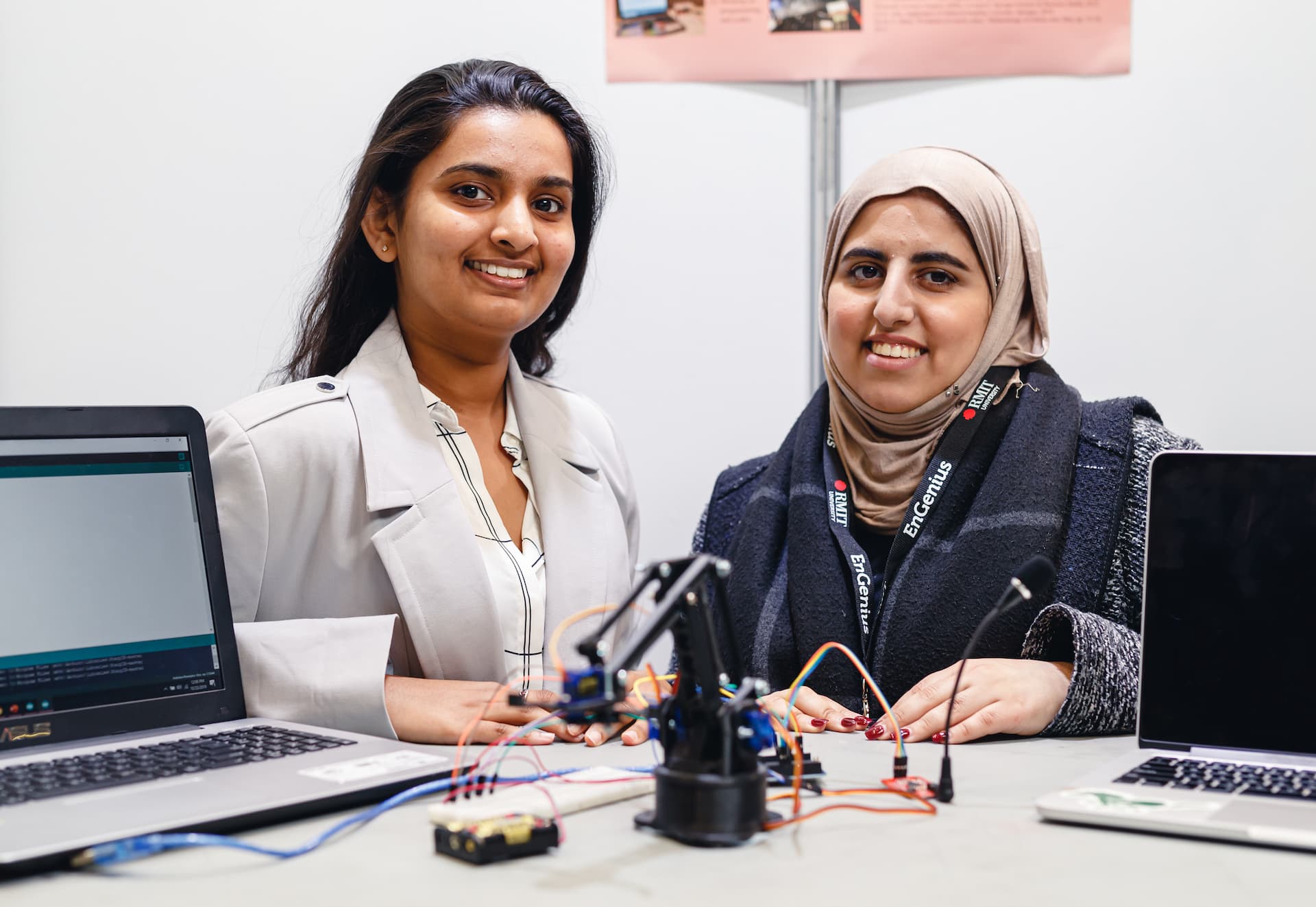 Two students smiling with with small robotics connected to laptops