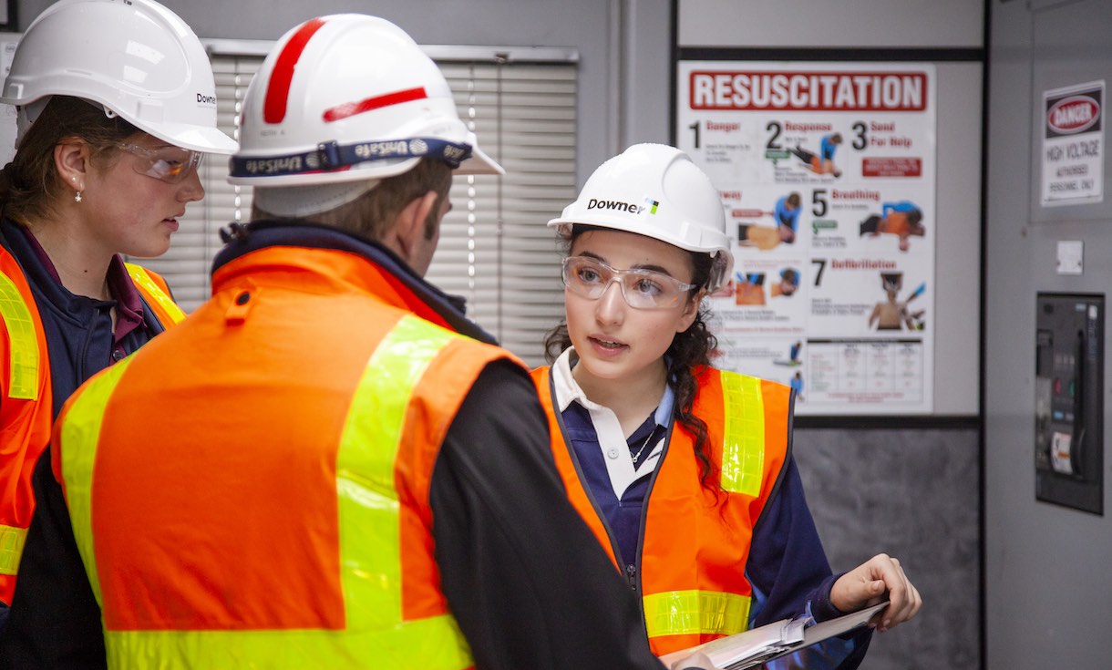 two female high school students in work gear talking to staff member on excursion to asphalt plant