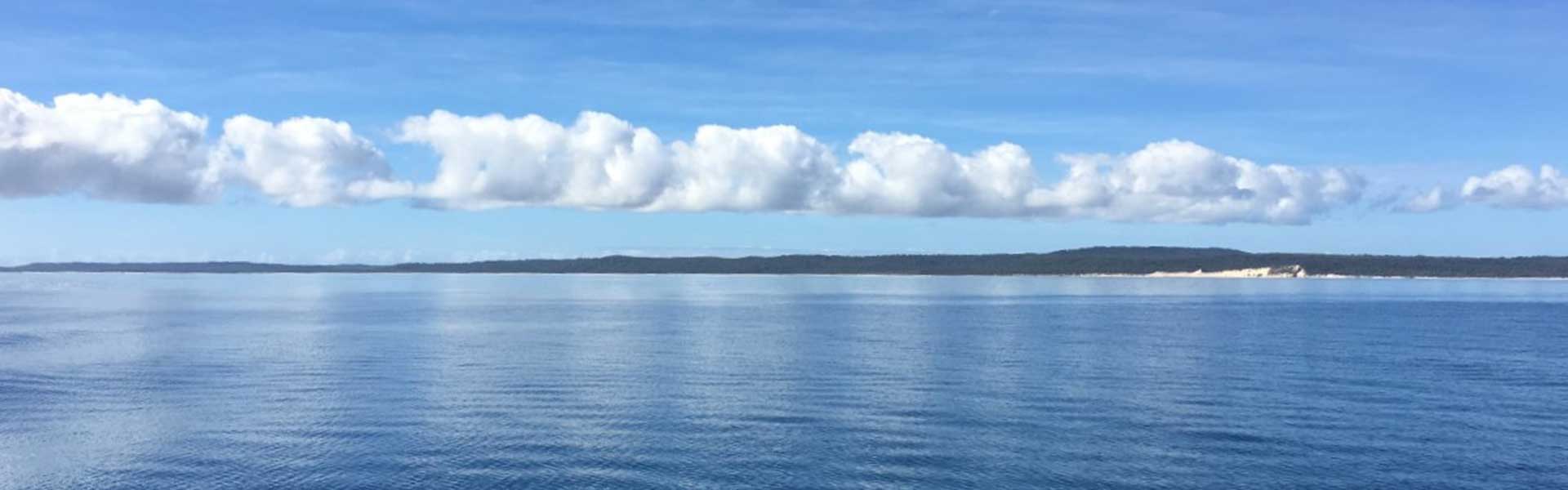 distant island with ocean in the forefront and white clouds in a blue sky 