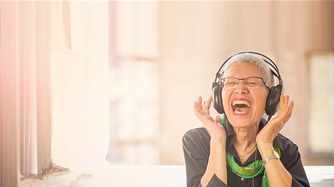 Senior old woman listening to her favourite music through big headphones, enjoying the rich sound