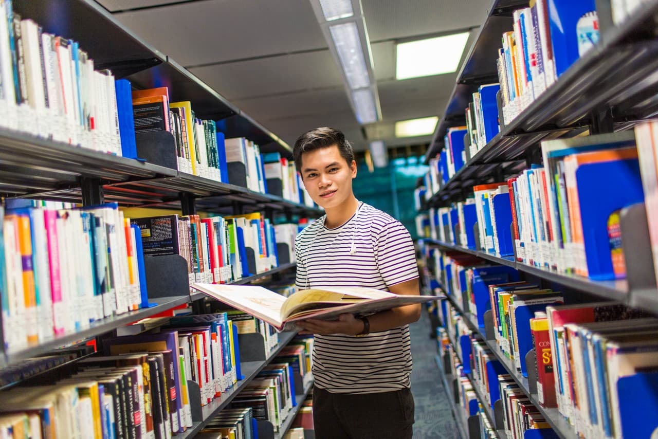 An RMIT student holding a book while standing in between bookshelves in a library.