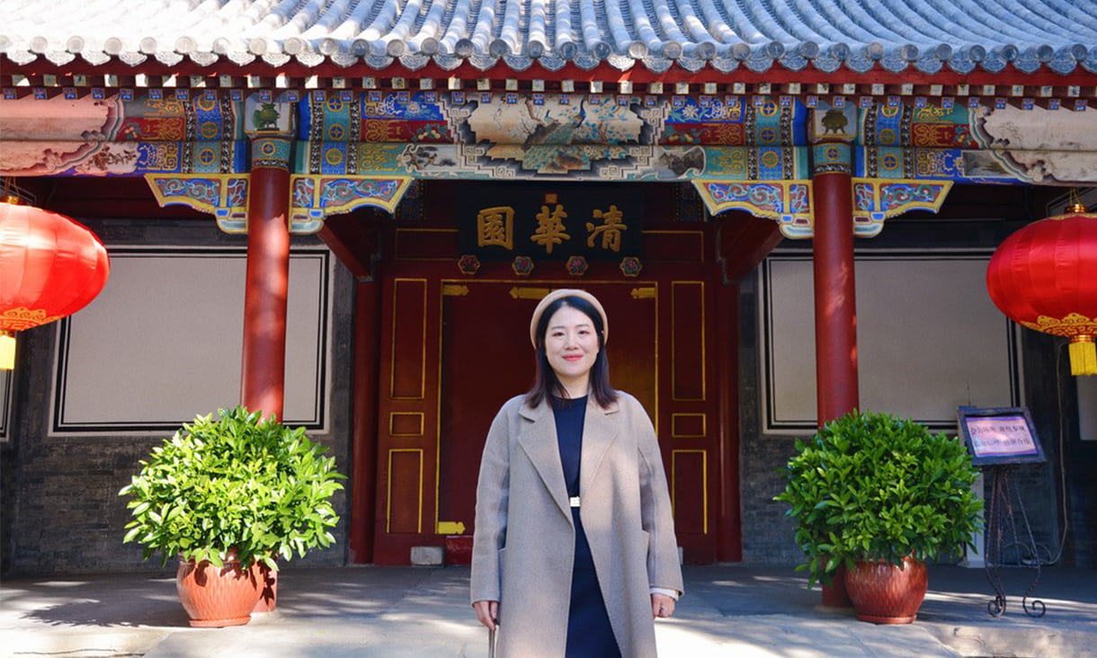 RMIT Chinese alumni Jing Wei standing infront of a shrine with lanterns wearing a long grey coat.