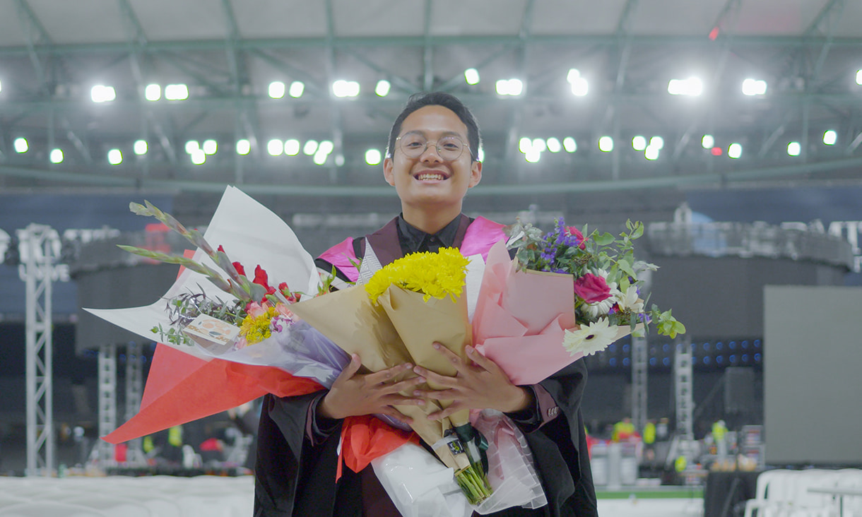 Raffa Pramata holding bunches of flowers after his graduation ceremony at RMIT