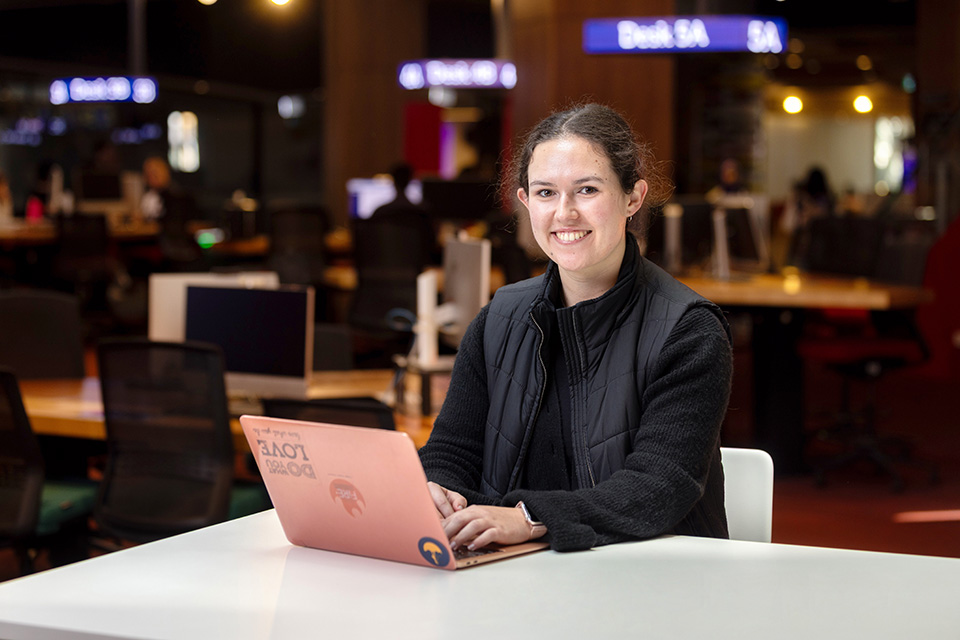 A girl at her laptop smiling at the camera.