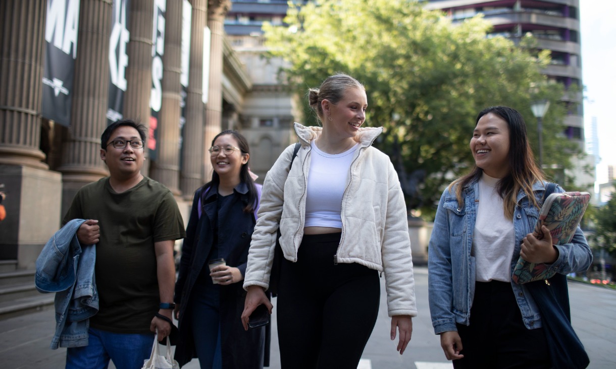 Group of four students walking in front of the state library while smiling