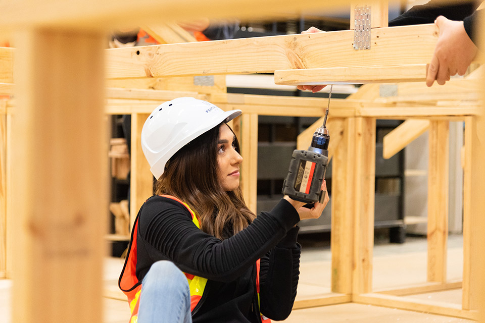 Female trades student using powerdrill on wood frames