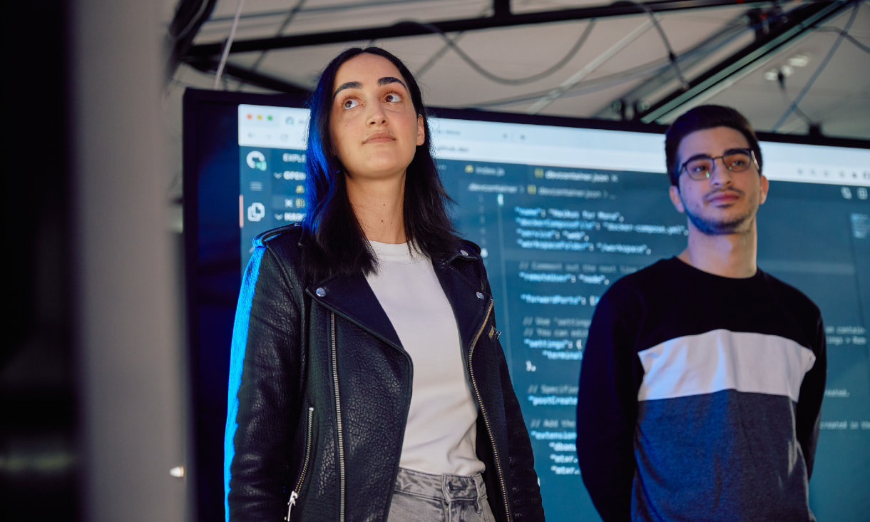 Female and male IT students standing in front of screen displaying code