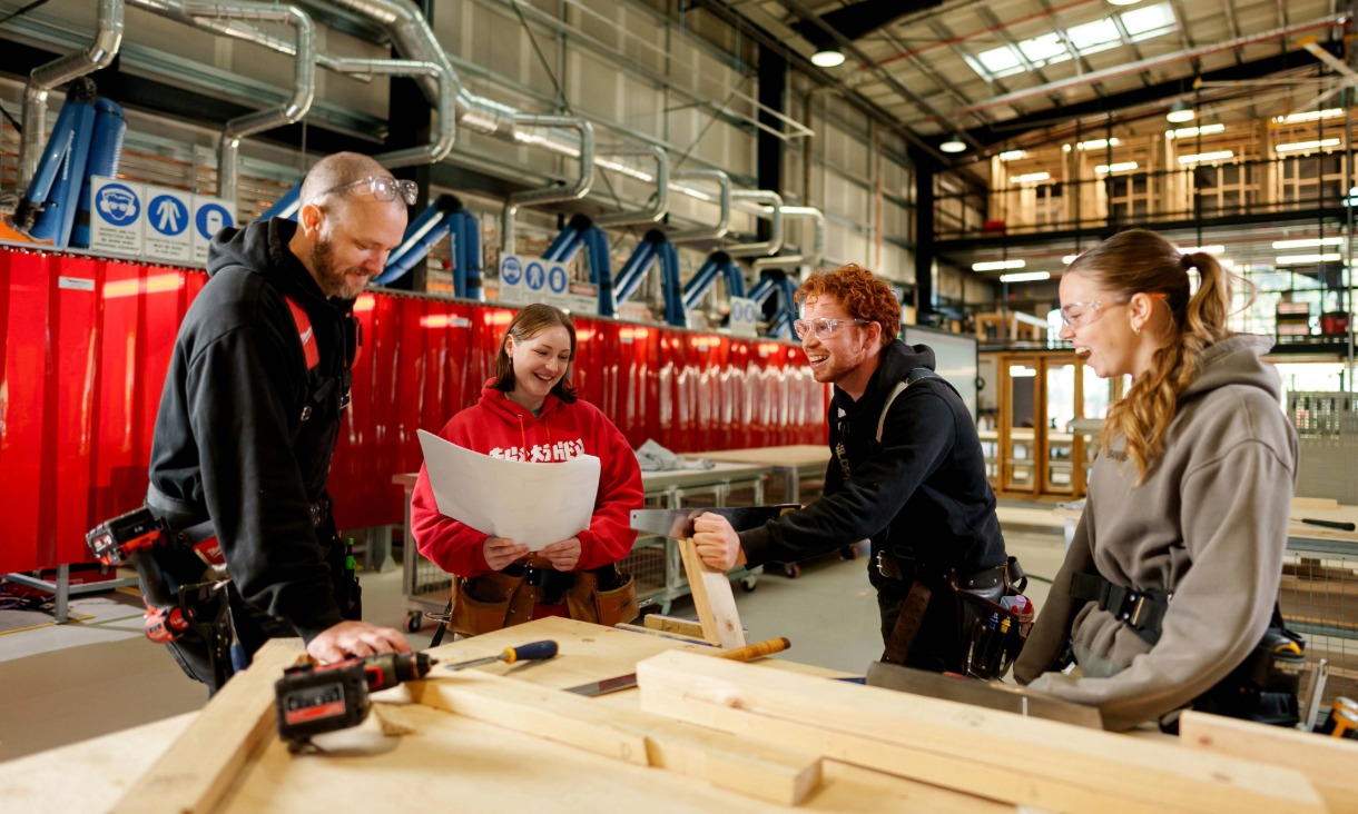 Four people collaborate on a woodworking project in a workshop.